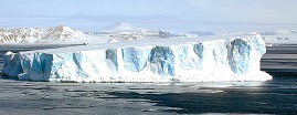Photo of a flat-topped iceberg surrounded by ice-pans, with the low mountains of Snow Hill Island in the distance.