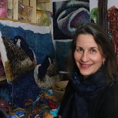 Photo. Mita Giacomini, with some of her artwork in the background.